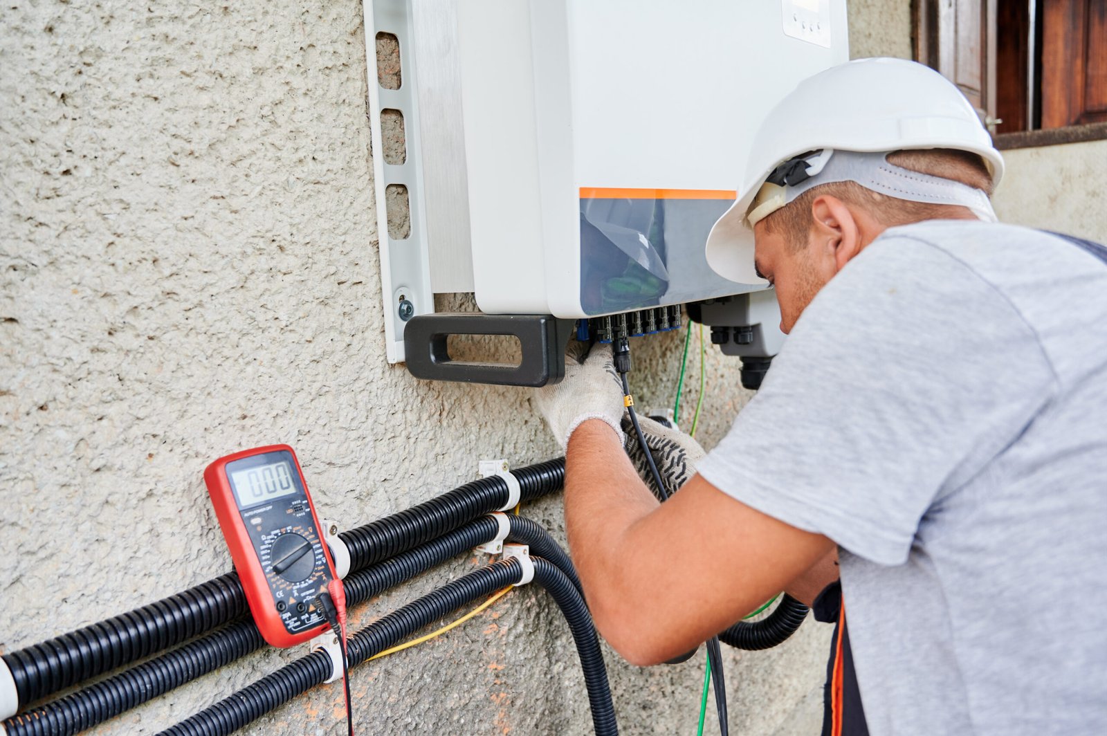 Man electrician installing solar panel system. Technician in helmet and gloves making electrical wiring inverter and electric box. Concept of alternative and renewable energy.